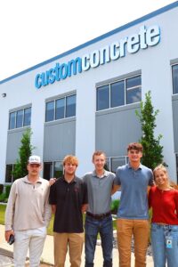 Interns posing in front of Custom Concrete building
