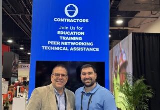 Two men stand in front of a Concrete Foundations Association banner at a convention.