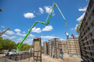 Forms for pouring a concrete foundation are set up for a building with a tall green crane overhead.
