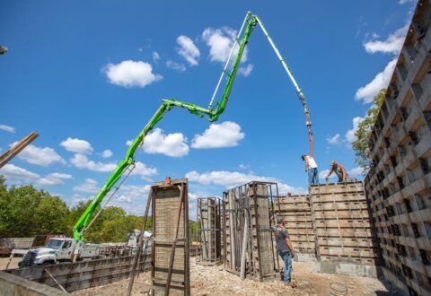 Forms for pouring a concrete foundation are set up for a building with a tall green crane overhead.