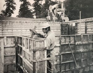 Black and white photo of the past, a young man levels concrete foundation walls.
