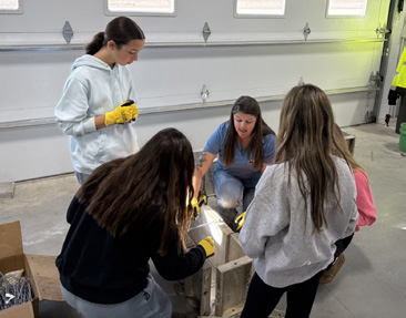 Un grupo de estudiantes practica la construcción de paneles de treinta centímetros de largo en círculo, con un miembro del equipo de Modern Poured Walls impartiendo formación práctica.