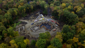 Aerial view of a building foundation in a forest will fall colors, circled by various construction vehicles.