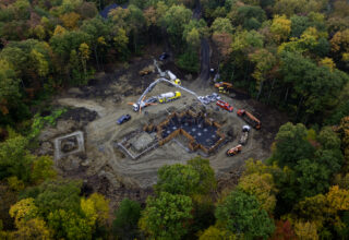 Aerial view of a building foundation in a forest will fall colors, circled by various construction vehicles.