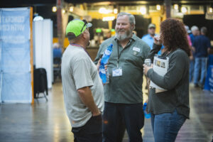 Three people stand and talk at a convention.