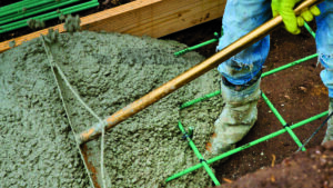 Construction worker spreading concrete in a form with wood and green tendons in a grid pattern.