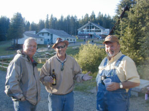 Three men stand with drinks in front of a house that is under construction in the forest