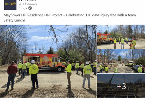 Social media post from N S Giles. Text: Mayflower Hill Residence Hall Project - Celebrating 130 days injury free with a team Safety Lunch!" 14 construction workers in flourescent yellow and hard hats wait for lunch at a food truck. On the right side are previews of three more photos with a plus 3 at the bottom showing even more.