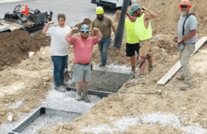 Six construction crew members stand in a concrete construction project. Three of them are curling their arms to show their biceps.