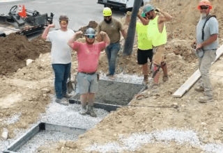 Six construction crew members stand in a concrete construction project. Three of them are curling their arms to show their biceps.