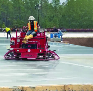 A construction worker riding a red power trowel smoothing wet concrete pavement.