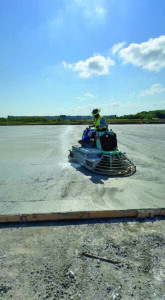 Construction worker riding a power trowel machine to smooth out wet concrete pavement.