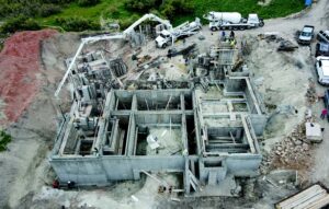 Aerial of concrete foundation walls for a multi-room building with a white crane overhead.